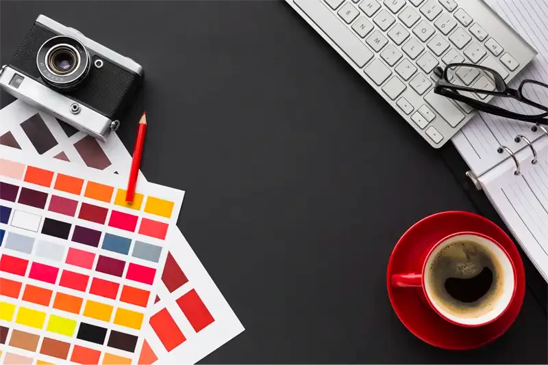 Desk with color samples, camera, keyboard, and coffee.